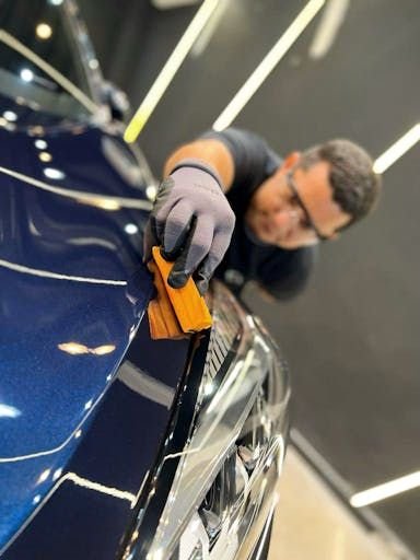 Detailer da Avanzati passando aplicador na pintura azul de um carro, sob luz de inspeção